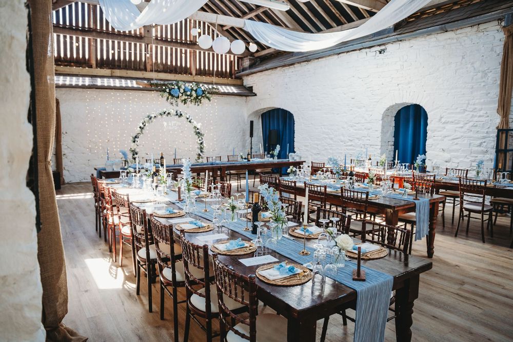 Elegant barn wedding reception with long wooden tables, floral arch, blue doors, and rustic exposed beam ceiling. Tan y Graig Aberystywth