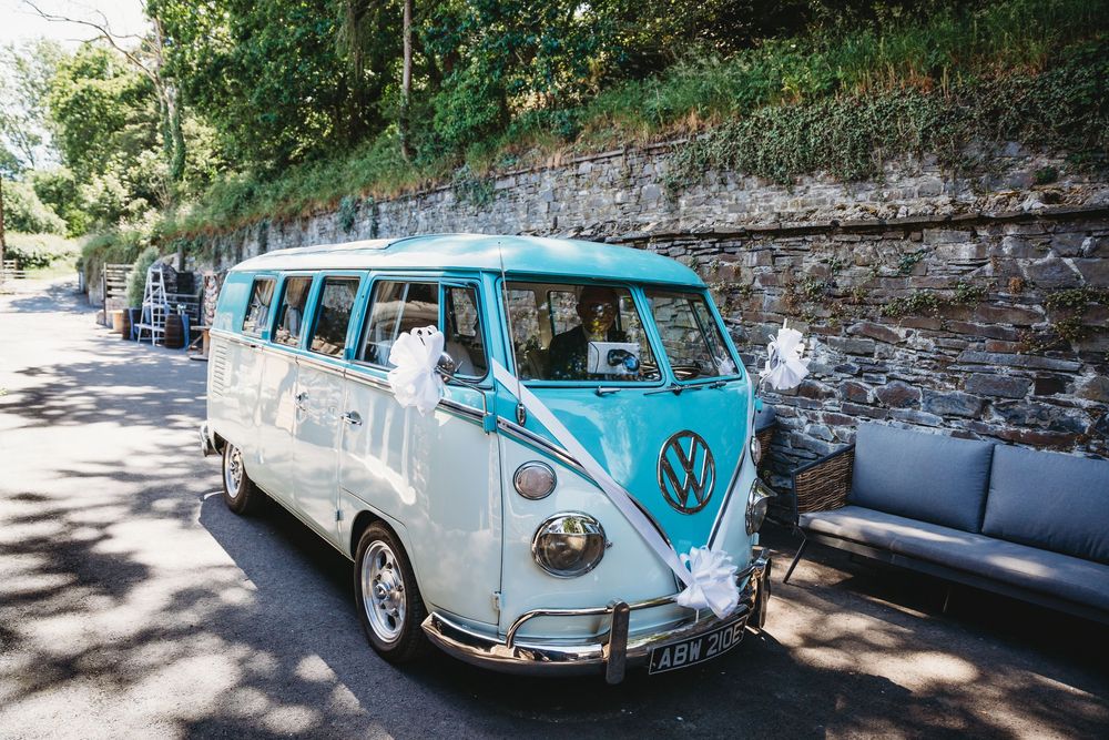Vintage teal and white VW camper van decorated with white ribbons parked outside for a wedding.