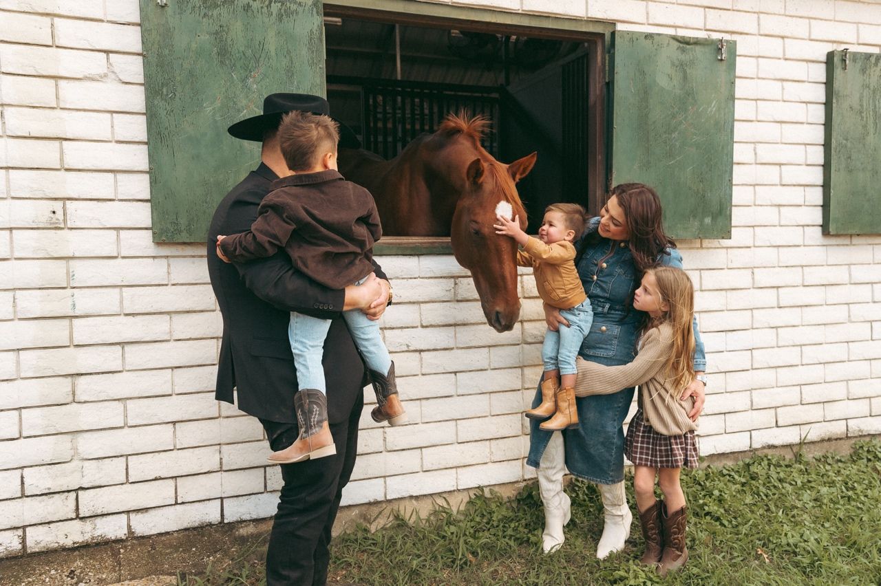 A family of five gathers at Windmill Stables in Richardson, TX greeting the horses in the barn.