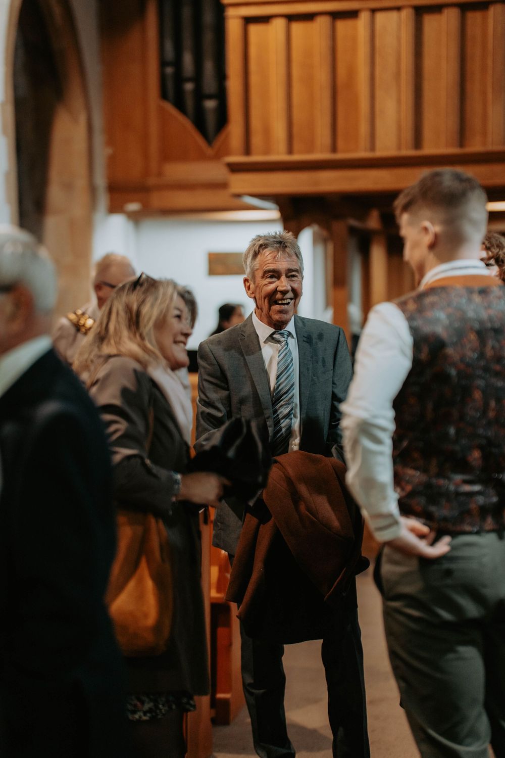Wedding guests socializing and laughing inside a church during a wedding ceremony.