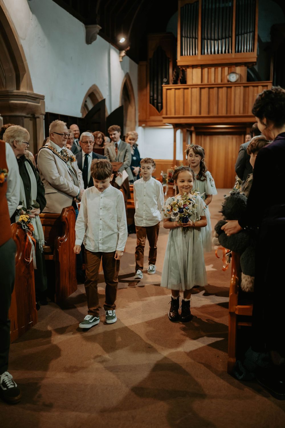 Children walking down church aisle at wedding ceremony, flower girl holding bouquet, guests seated in pews.