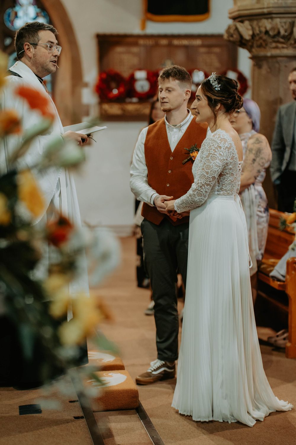 Bride and groom holding hands during a church wedding ceremony with a priest officiating.