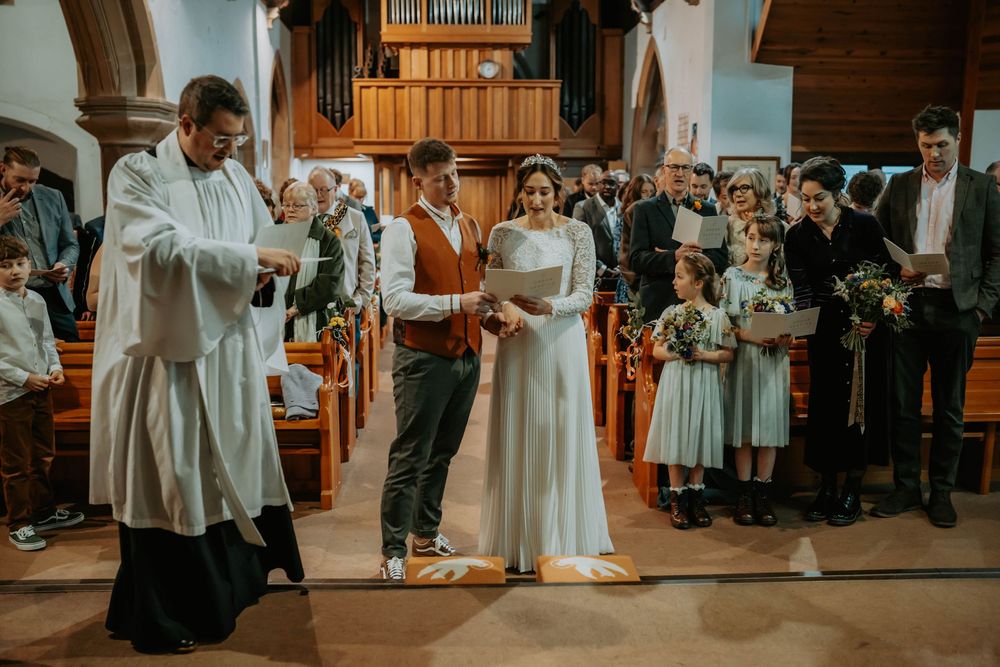 Bride and groom exchange vows at church altar with officiant, flower girls, and wedding guests in a traditional ceremony.