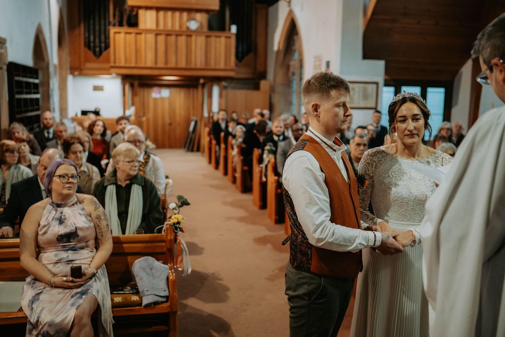 Couple exchanging vows at a traditional church wedding ceremony with guests seated in wooden pews.