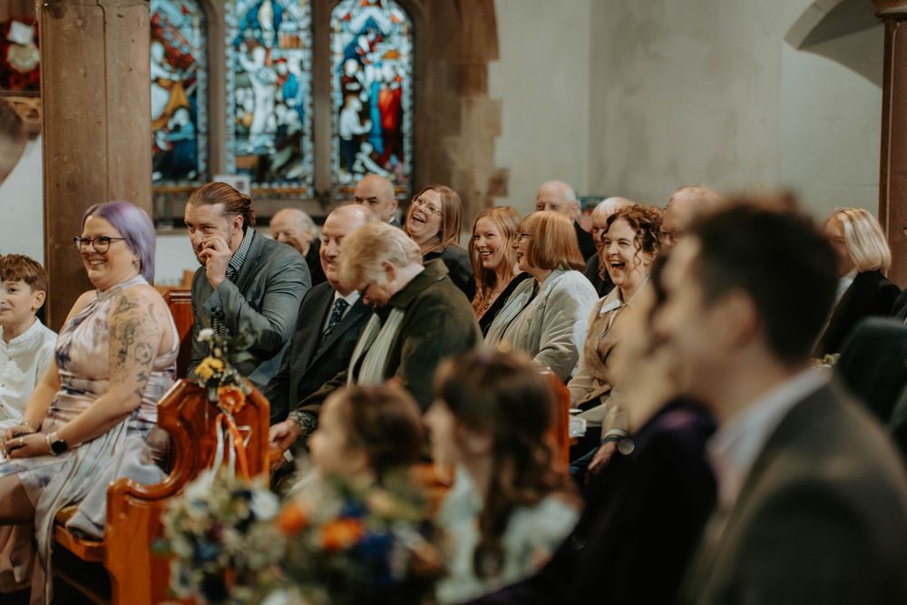 Wedding guests laughing and celebrating in a historic church with stained glass windows during a joyful ceremony.