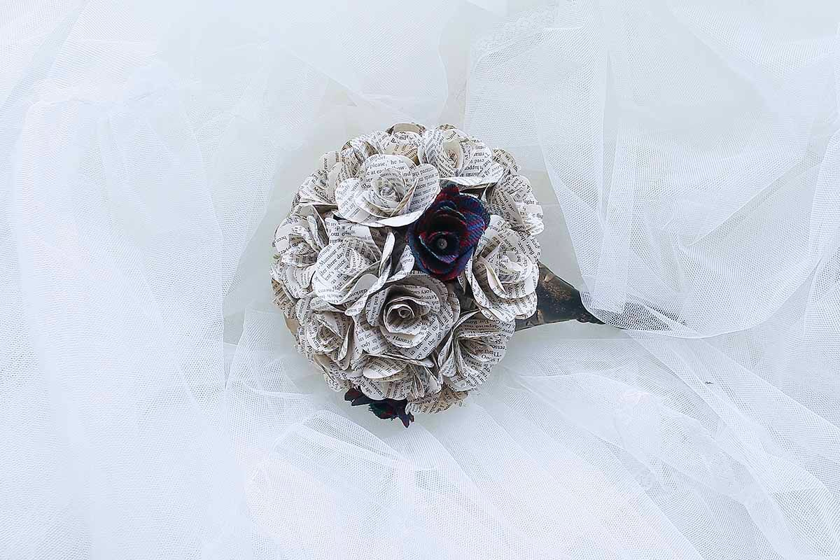 Handmade paper rose bouquet crafted from book pages with dark purple accents, resting on white tulle fabric.