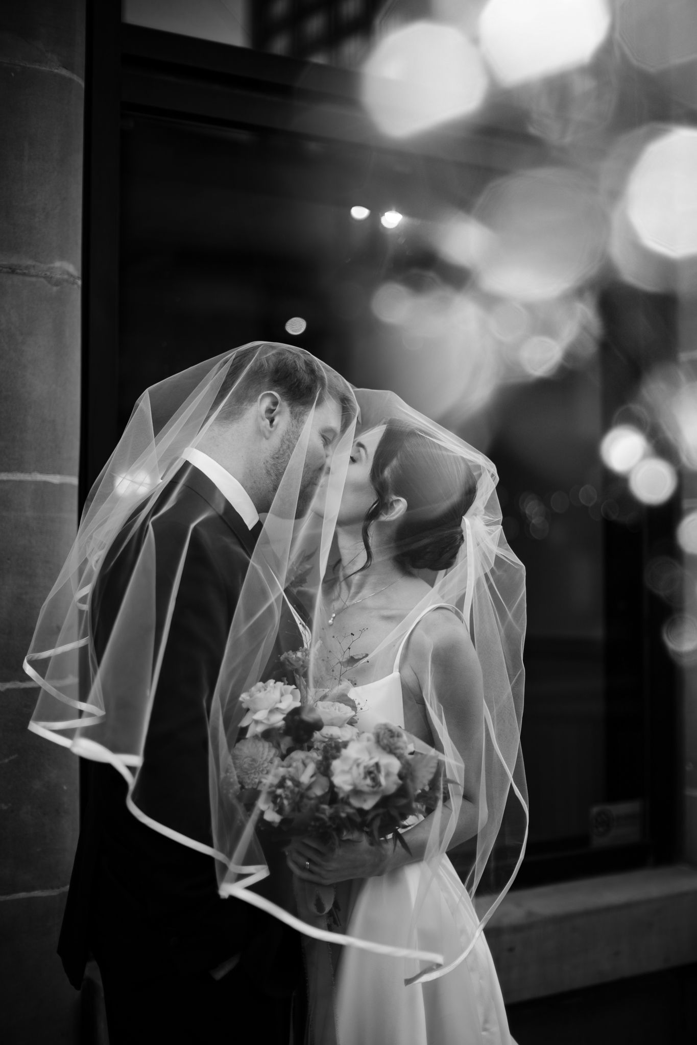 Black and white veil kiss with soft bokeh lights on a Calgary wedding day, photographed by Tkshotz