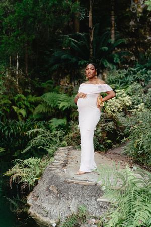 An expecting mother standing confidently on a rock near a body of water