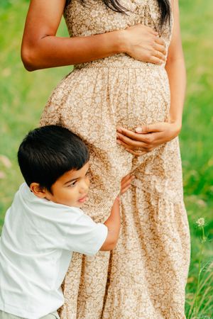 A son holds the leg of his pregnant mother