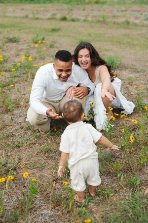 A mother and father cheer on their walking toddler
