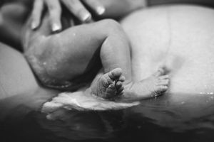 Black and white close-up of a newborn baby's tiny feet emerging in water during a birth.