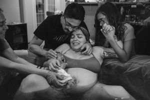 Black and white photo of a laboring woman in a birth pool supported by family members during a home water birth.