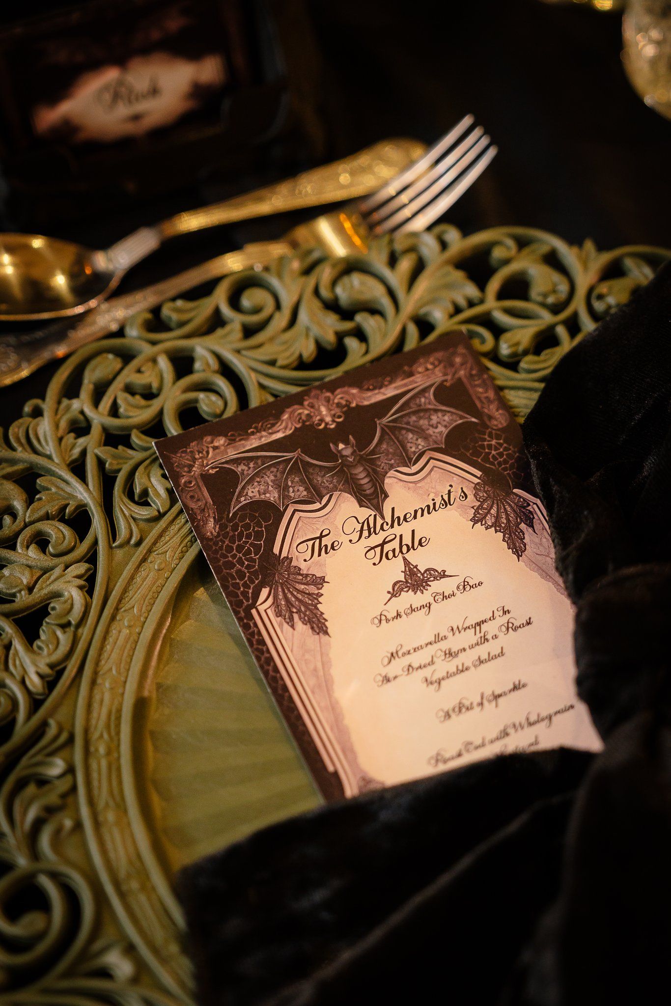 Gothic wedding menu titled The Alchemist's Table with bat illustrations on a gold charger plate