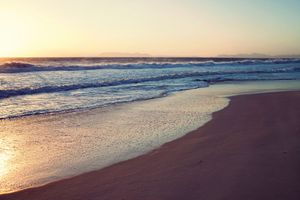 Serene sunset beach scene with gentle ocean waves washing onto golden sandy shore.