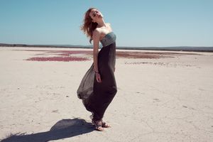 Woman in flowing dark maxi dress poses on vast white salt flat under clear blue sky.