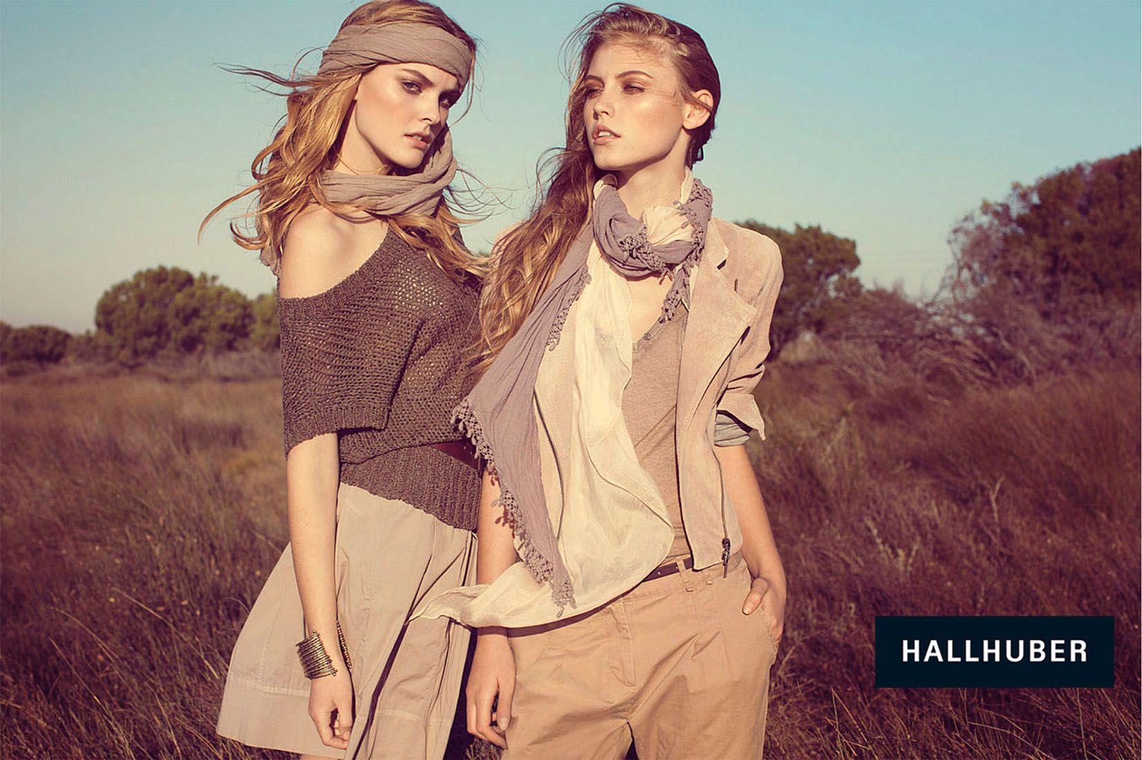 Two female models wear HALLHUBER autumn fashion in neutral tones standing in a golden field.