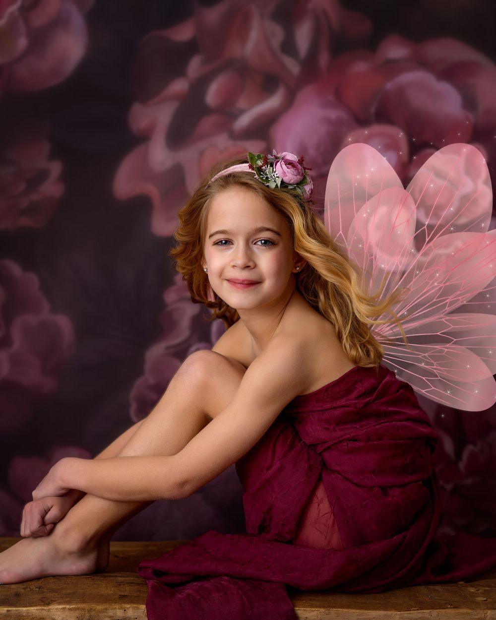A girl posed in front of a fine art background with wings and fabric