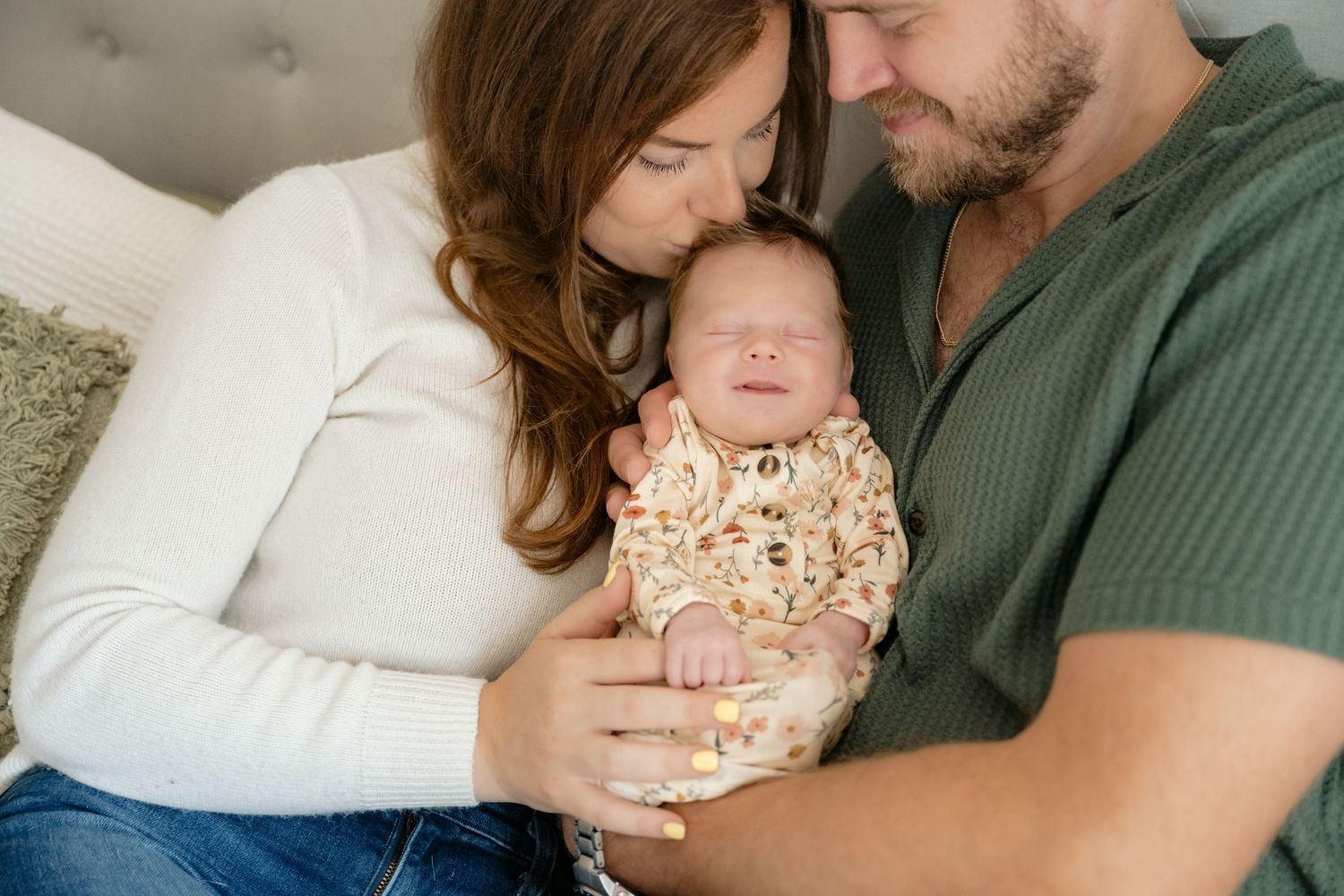 A closeup portrait of mom and dad holding their newborn baby while mom kisses baby's head during in-home lifestyle newborn portraits in MN.