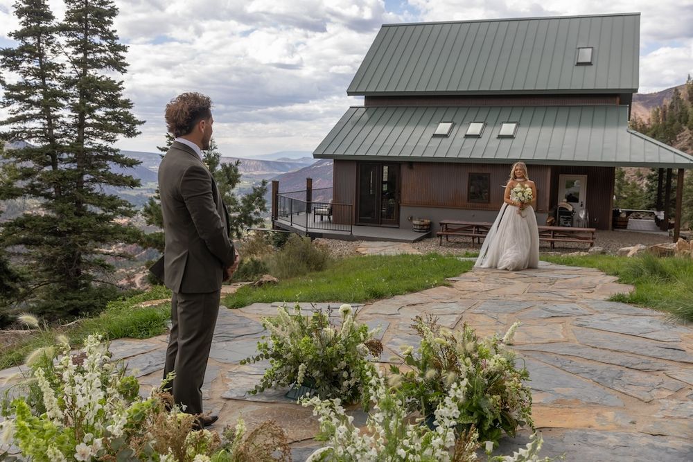 Bride and groom share first look moment on mountain stone patio with rustic cabin and scenic Colorado views.