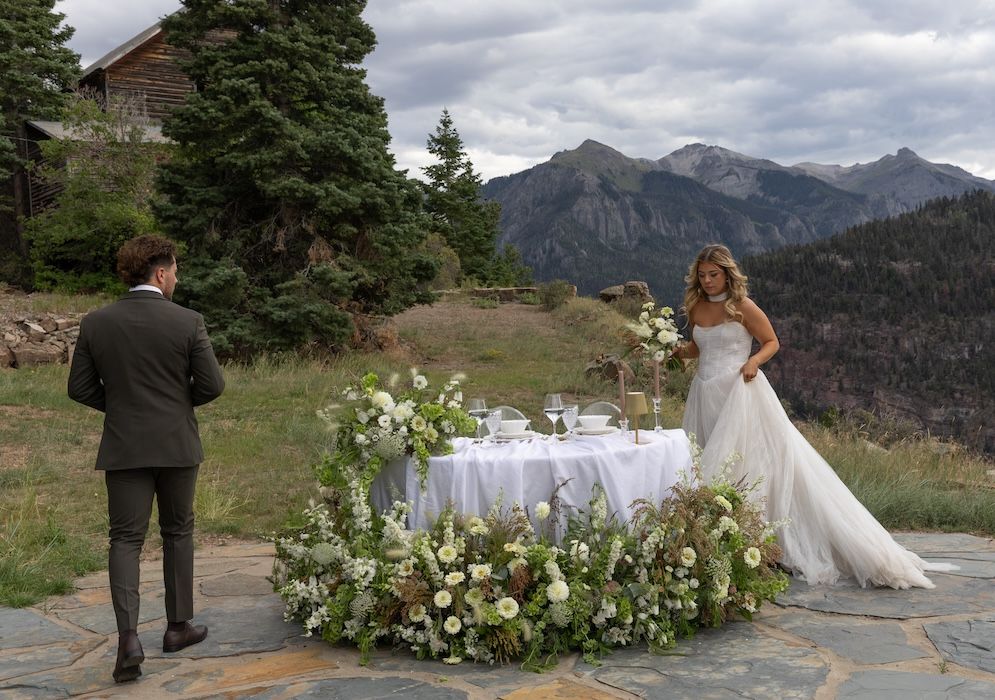 Bride and groom at outdoor mountain wedding ceremony with floral arrangements and scenic Rocky Mountain backdrop.