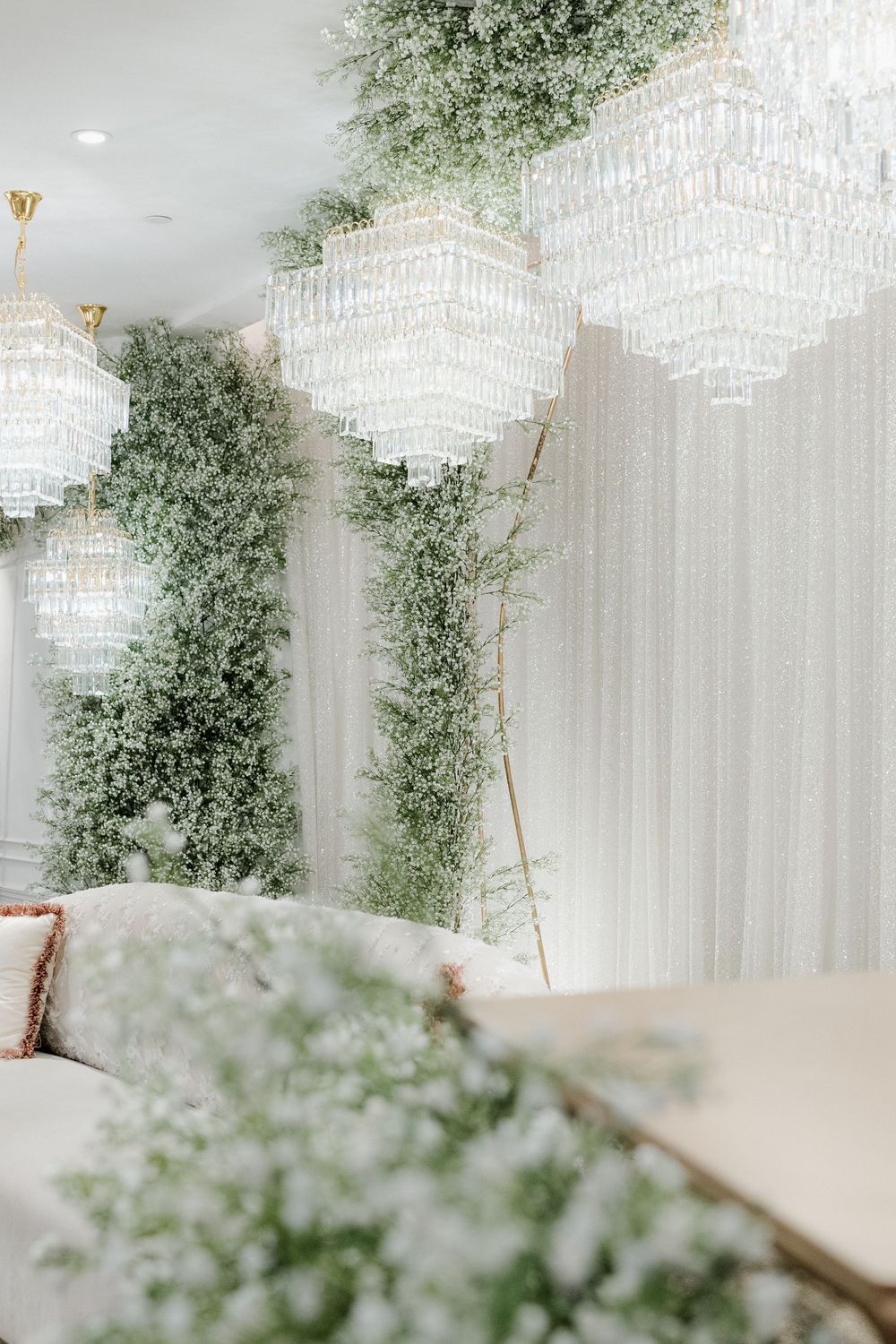 Elegant wedding venue with crystal chandeliers, lush greenery walls, and white decor creating a romantic atmosphere.