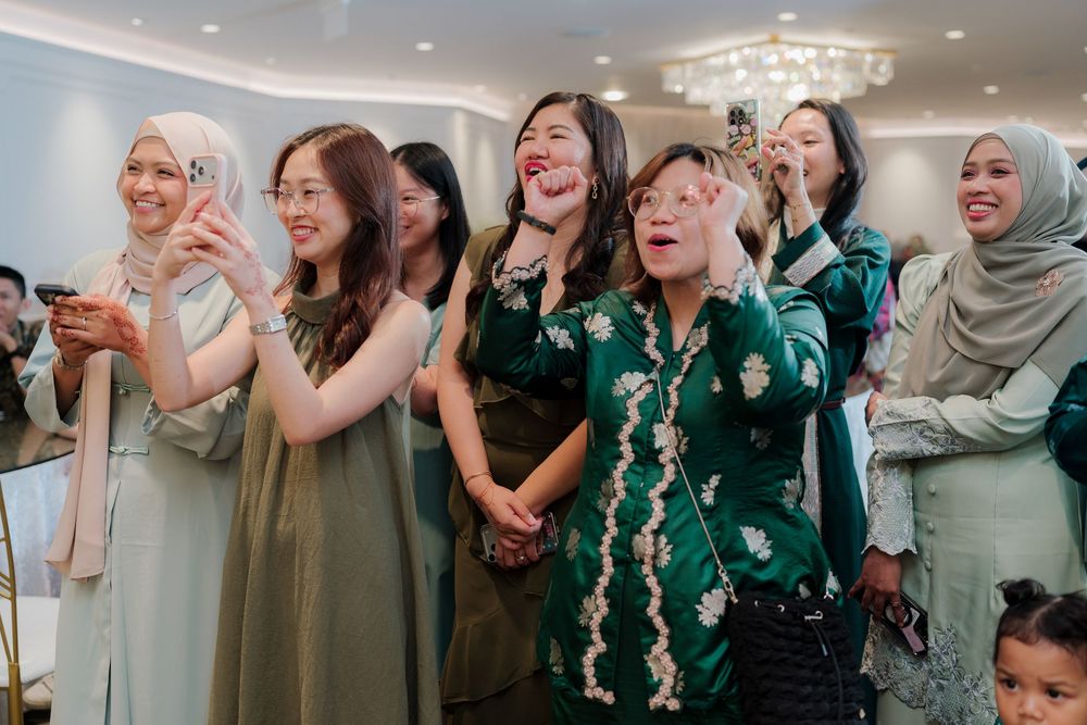 Diverse group of women in elegant attire joyfully celebrating at a wedding reception in a decorated hall.
