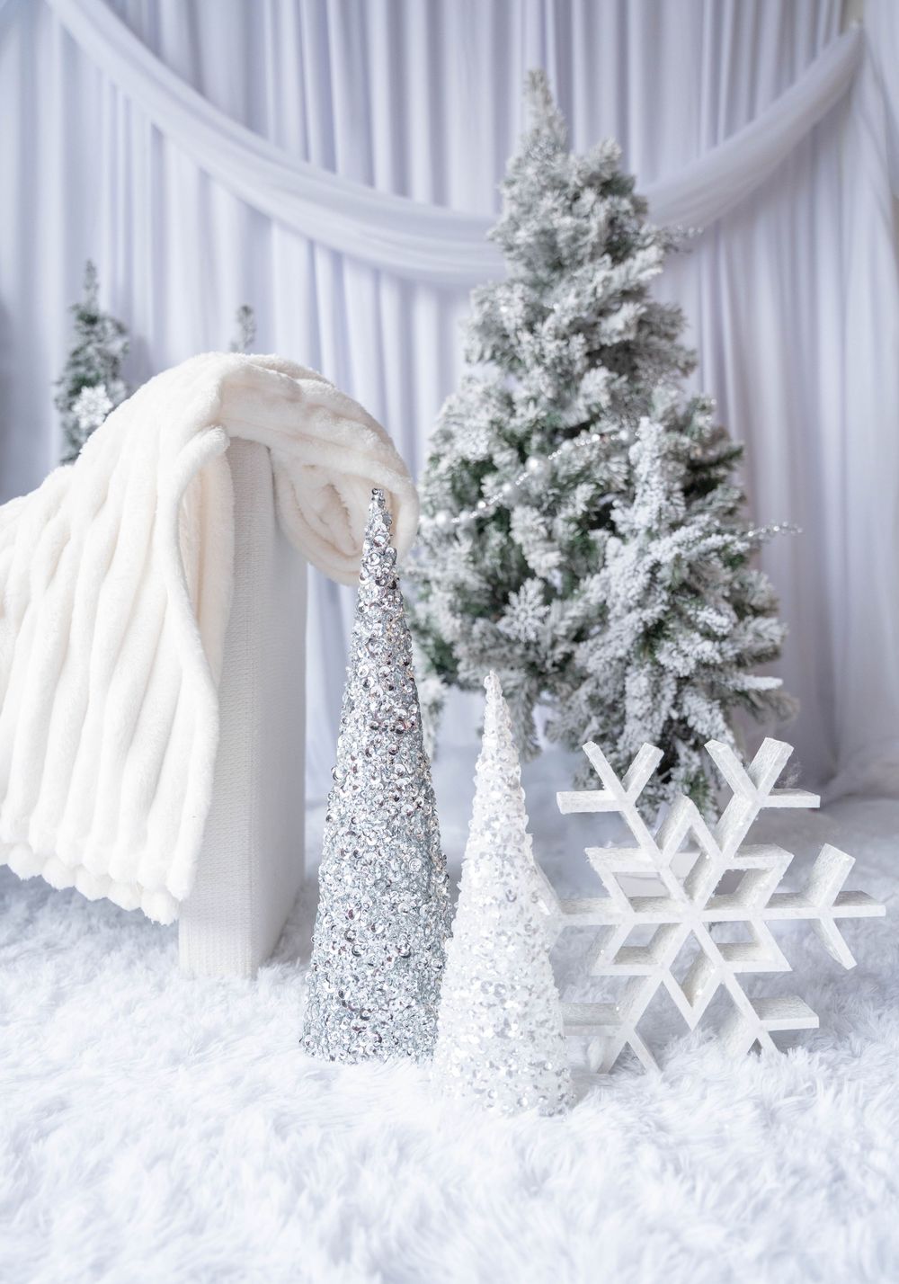 White winter wonderland Christmas scene with frosted trees, glittery cone trees, and a large decorative snowflake on faux fur.