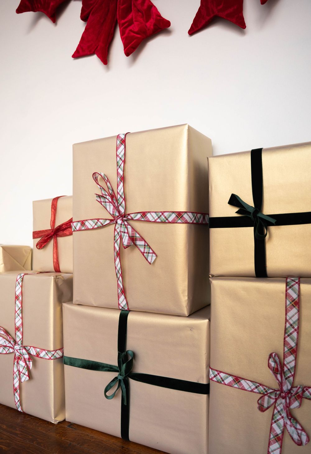 Stack of gold-wrapped Christmas gifts with colorful ribbons and bows, decorated with red poinsettia garland above.