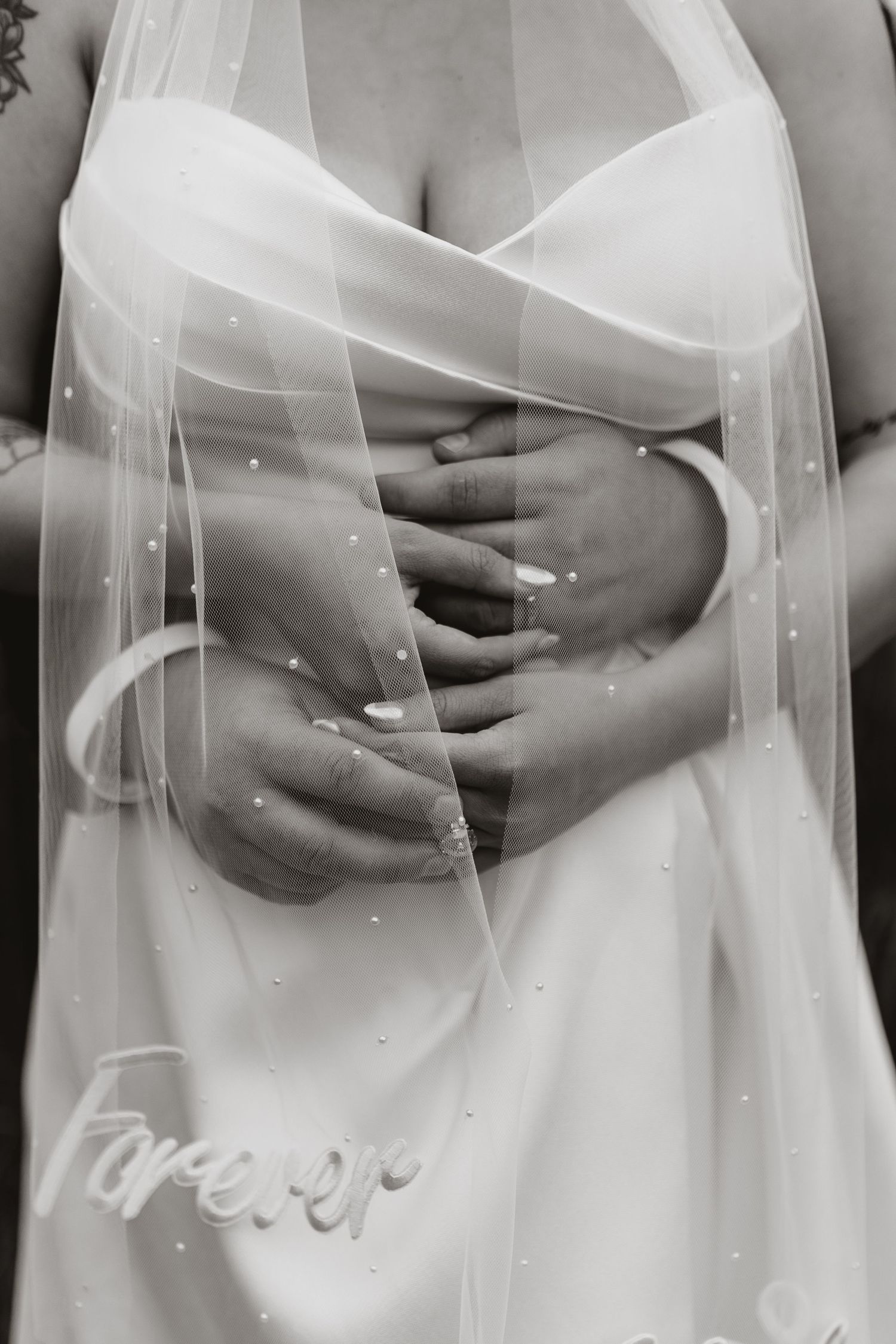 Black and white wedding photo of bride and groom holding hands, veil overlay with "Forever" script detail.