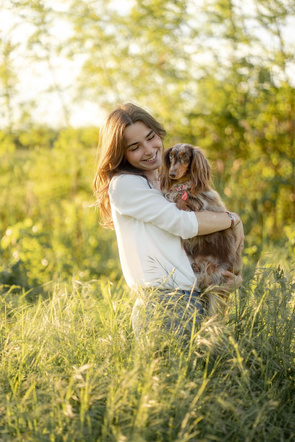 Jeune femme souriante tenant son chien teckel dans une prairie verdoyante baignée de soleil.
