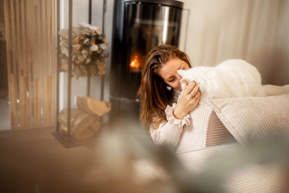 Woman relaxing on a couch near a fireplace, holding a warm drink in a cozy living room.
