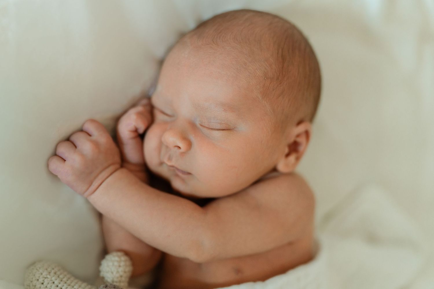Peaceful newborn baby sleeping curled up on soft white blanket in professional newborn photography portrait.
