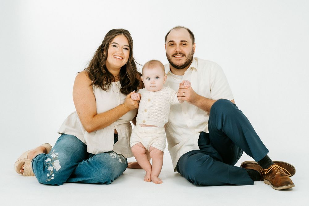 Happy family portrait with parents and baby sitting on white background in casual outfits.