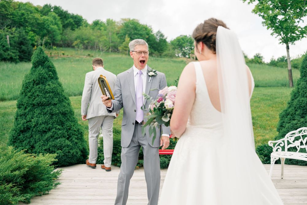 Father of the bride reacts with joy seeing daughter in wedding dress outdoors at elegant garden venue.