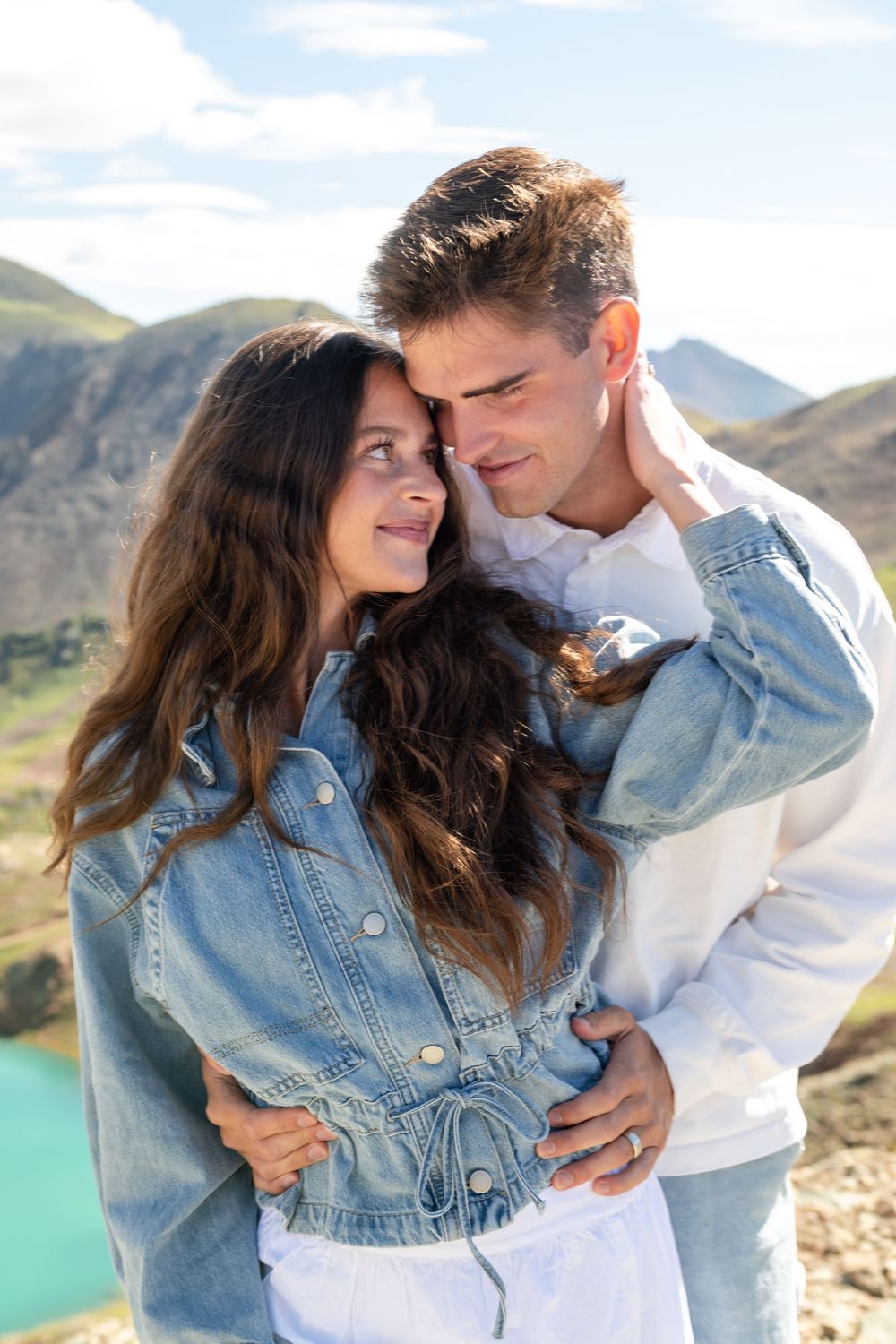 Couple embracing and gazing at each other with mountain backdrop on a sunny day.