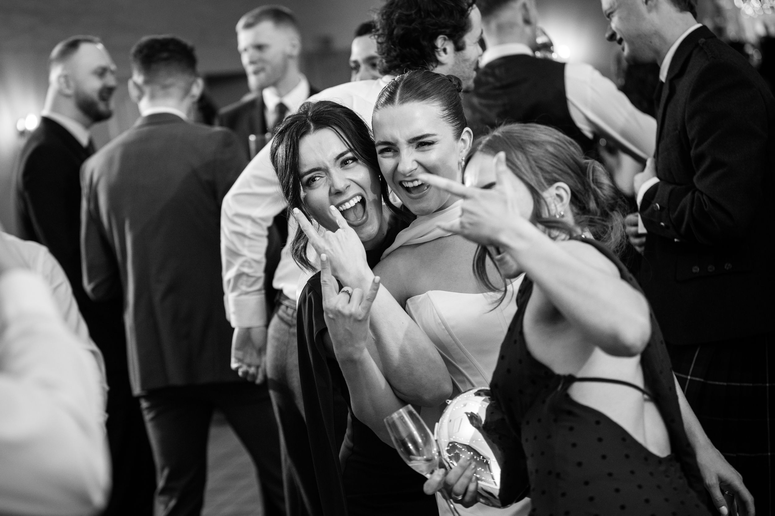 Black and white photo of three women laughing and posing together at a wedding reception party.