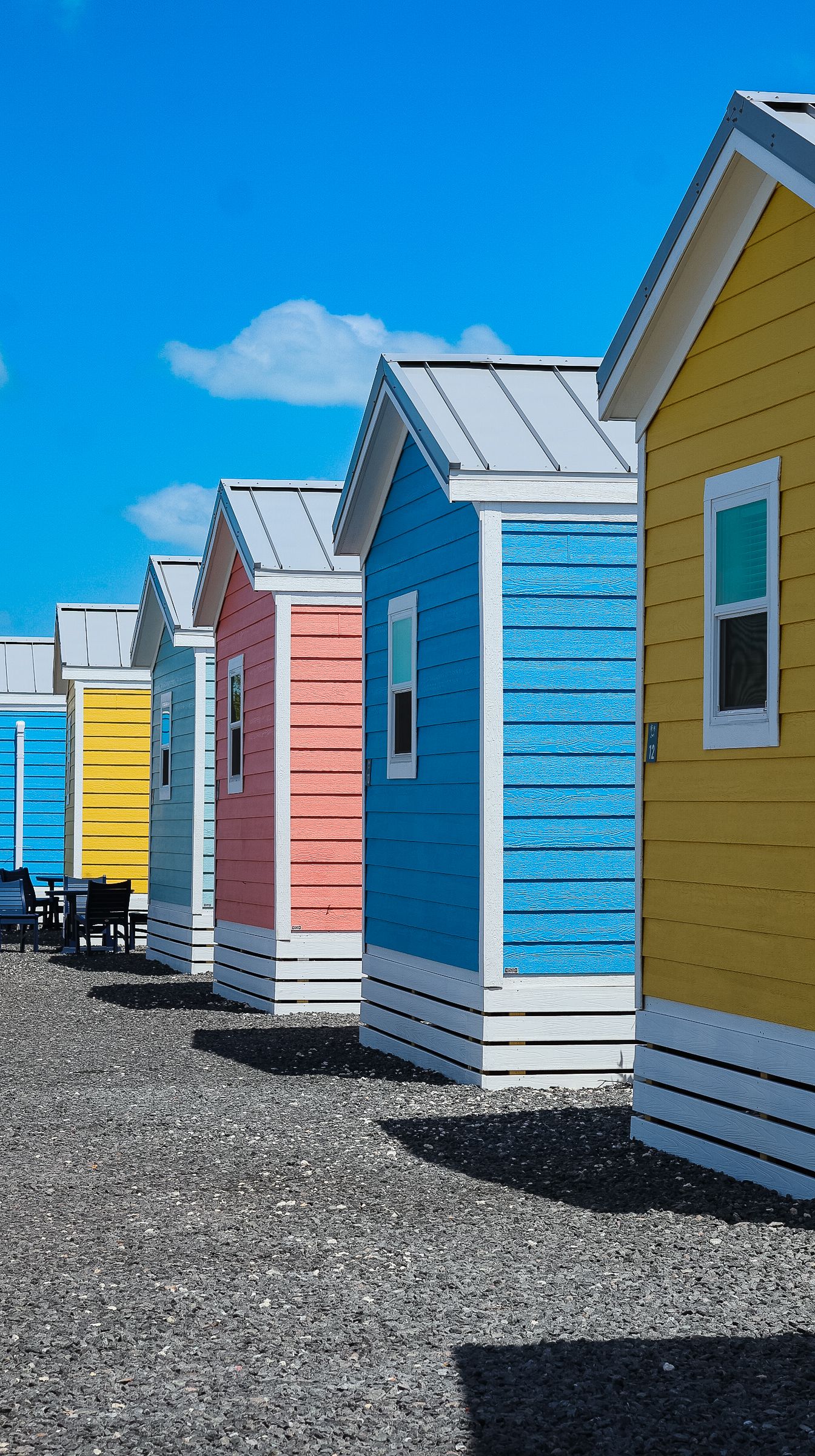 Row of colorful tiny cabin rentals in yellow, blue, and red under a bright blue sky on gravel.