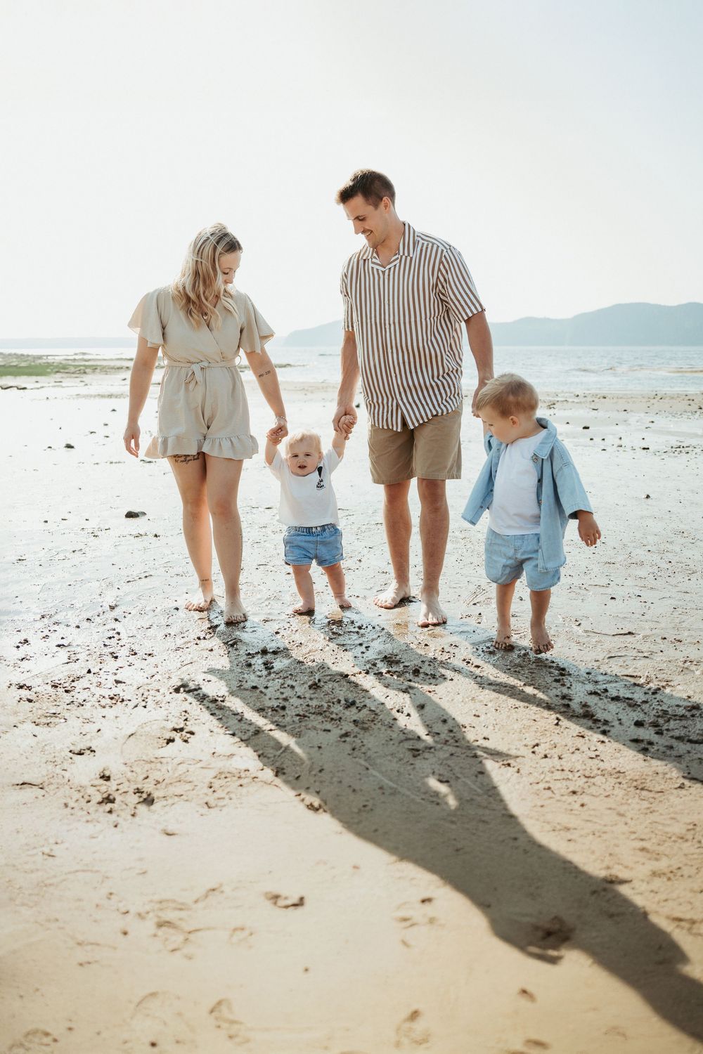 Happy family with two young children walking together on a sunny beach.