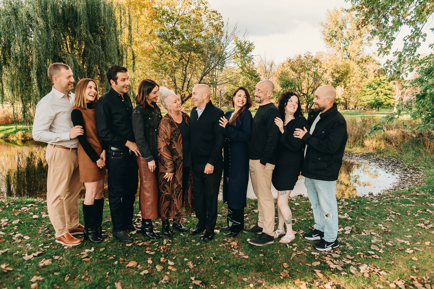 Family group photo outdoors in autumn park with colorful fall foliage and pond in background.