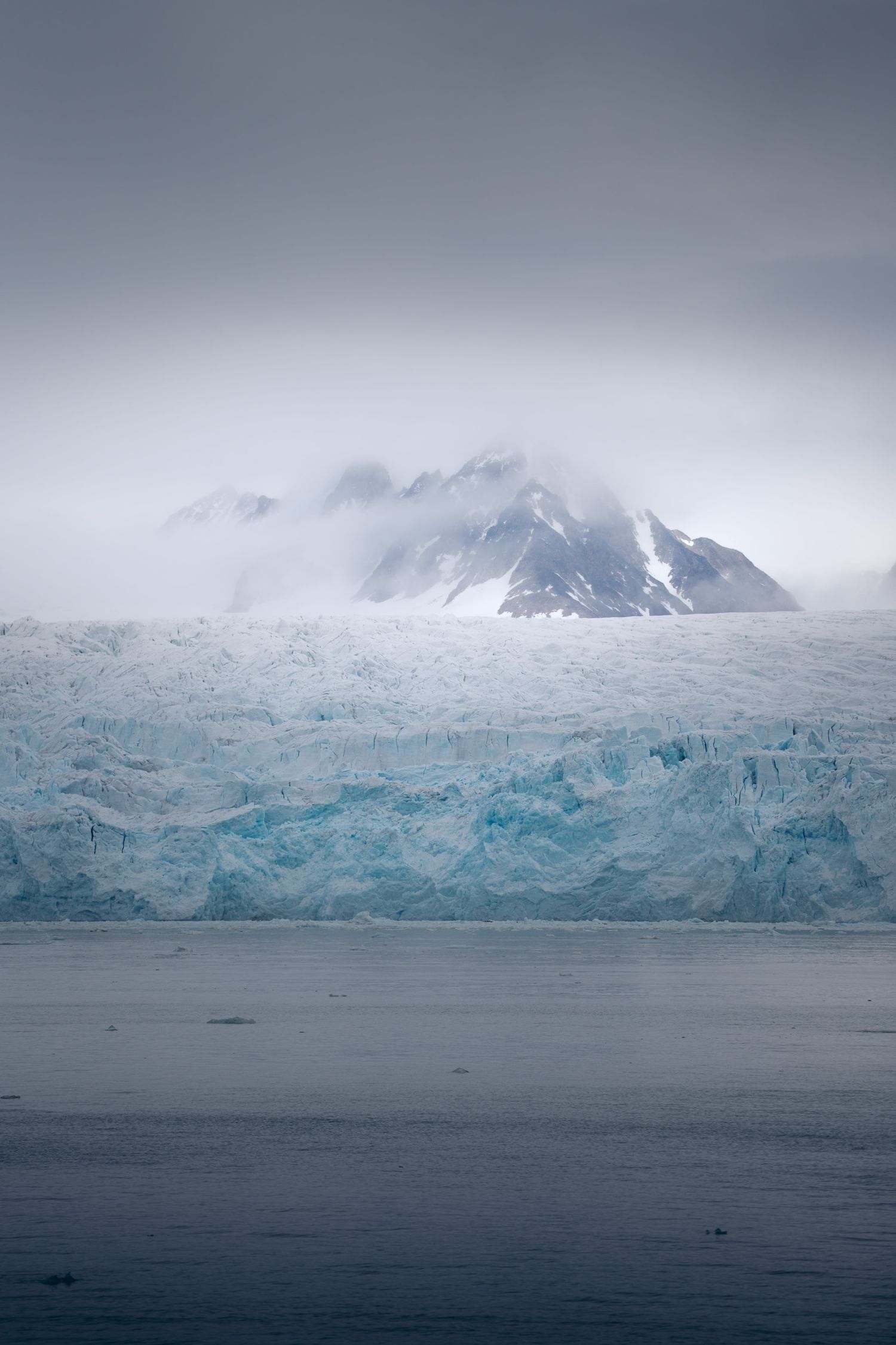 Montagne noire émergeant du brouillard au-dessus d'une muraille de glace, au Svalbard