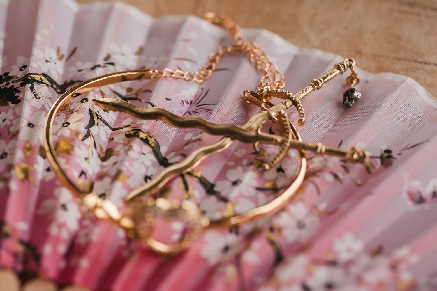Close-up of the bride's gold sword-shaped earring and heart bracelet on a floral fan, a subtle nod to her love of fantasy.