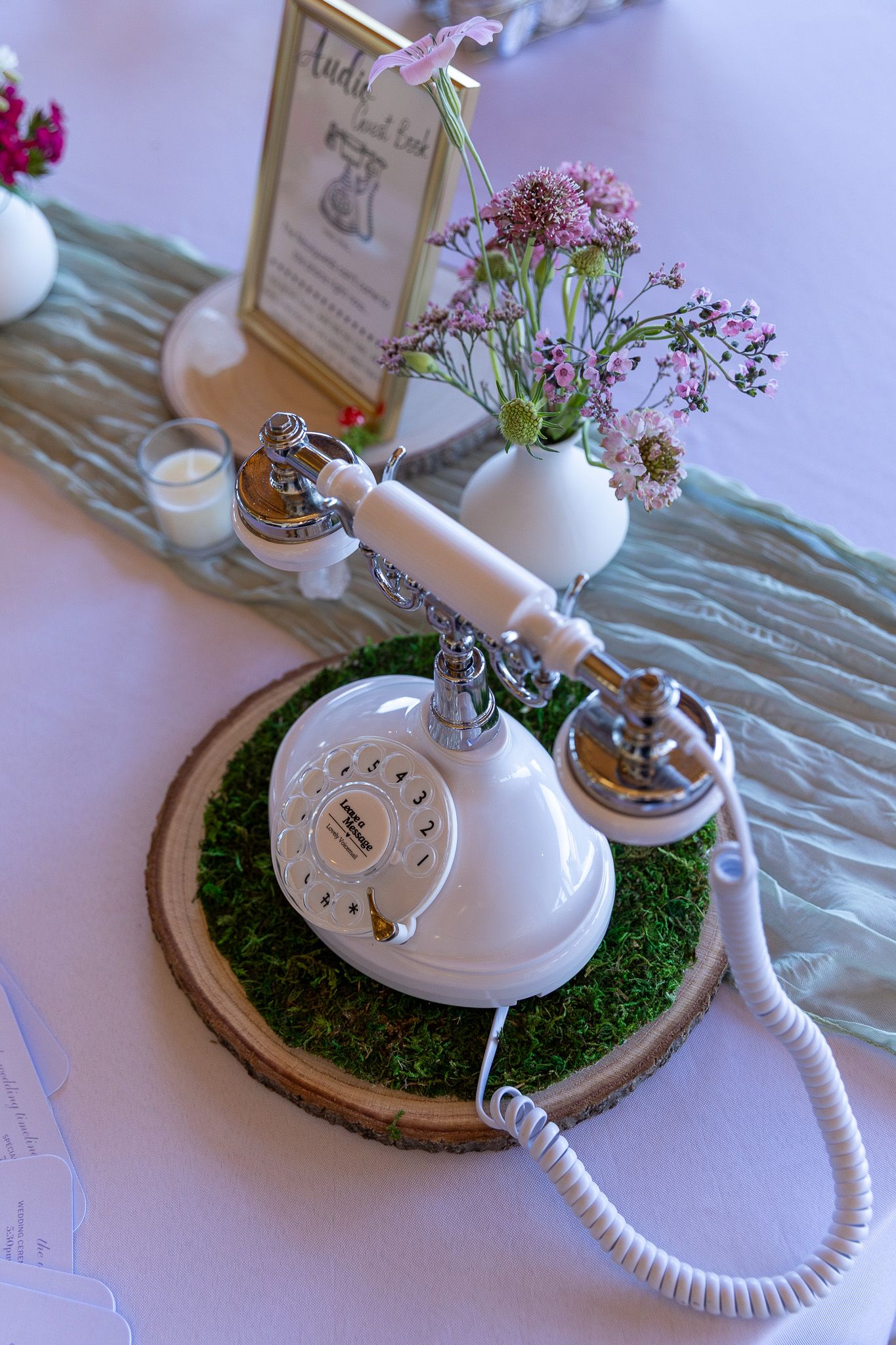 Vintage white rotary phone on moss-covered wood slice centerpiece with pink wildflowers at wedding reception.