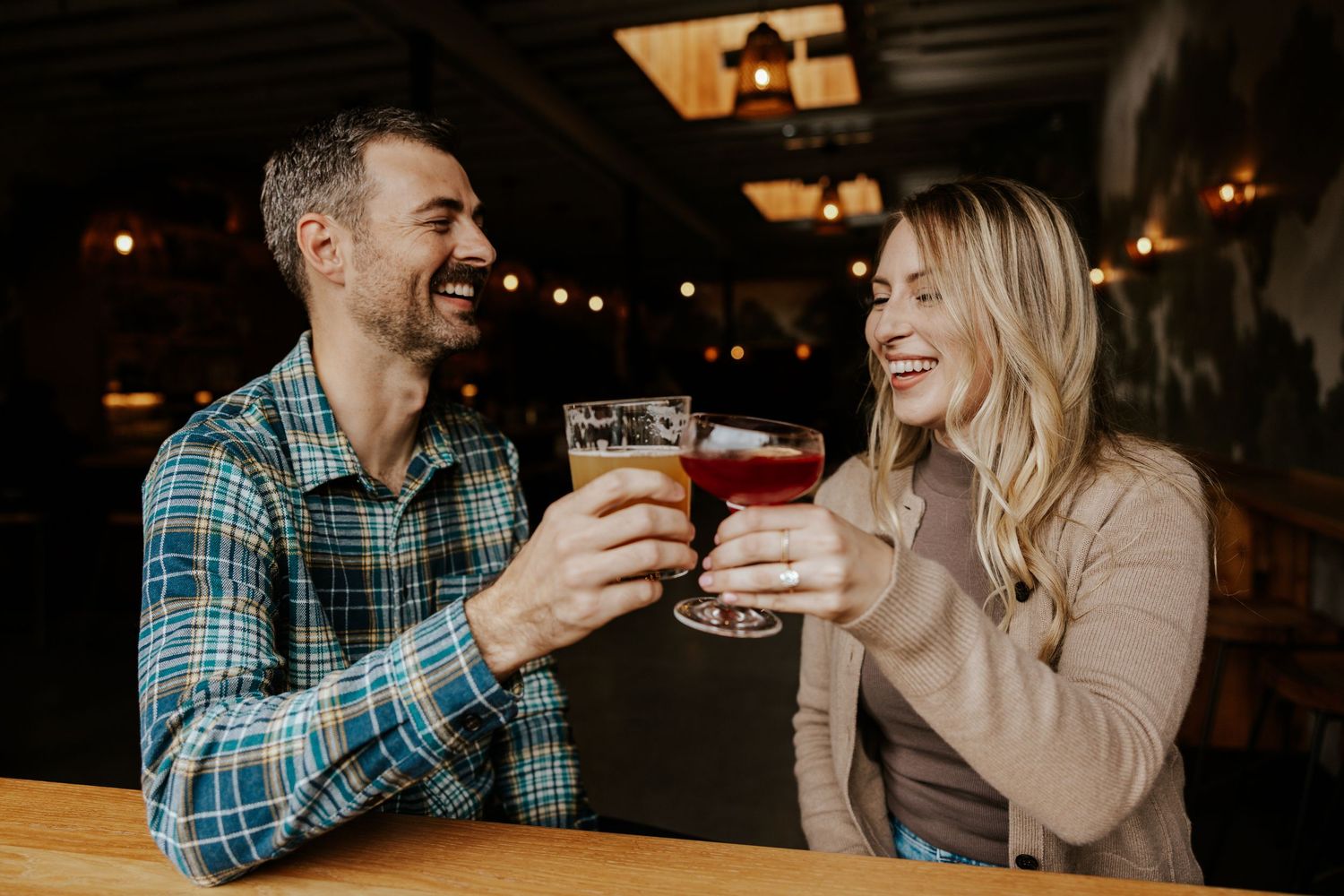 playful couple clinking their beer and cocktail at a bar during san francisco engagement photoshoot