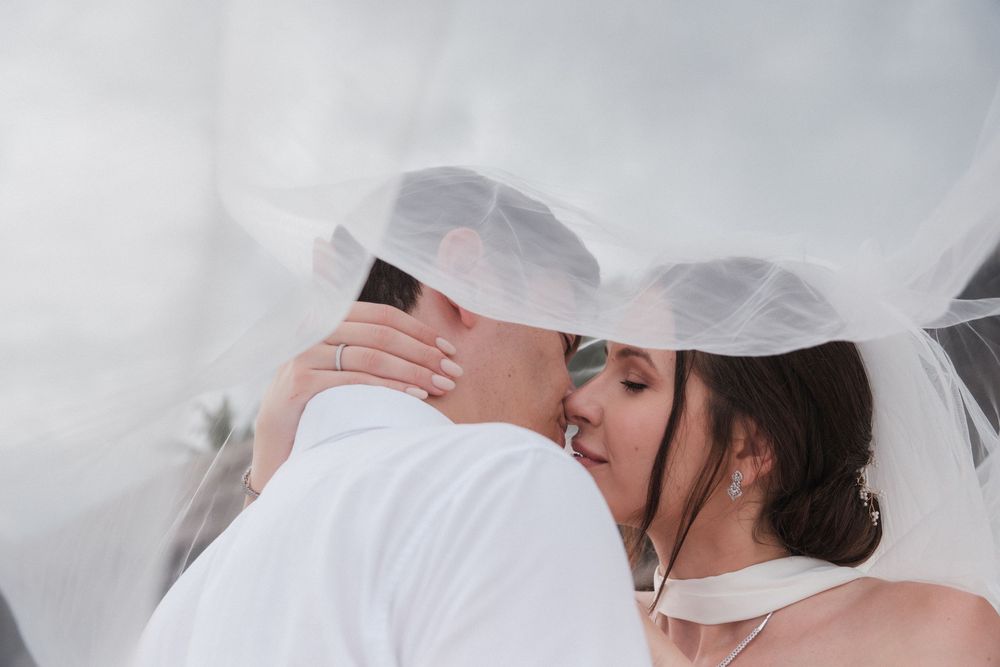 Bride and groom sharing a romantic kiss under a flowing white wedding veil on their special day.