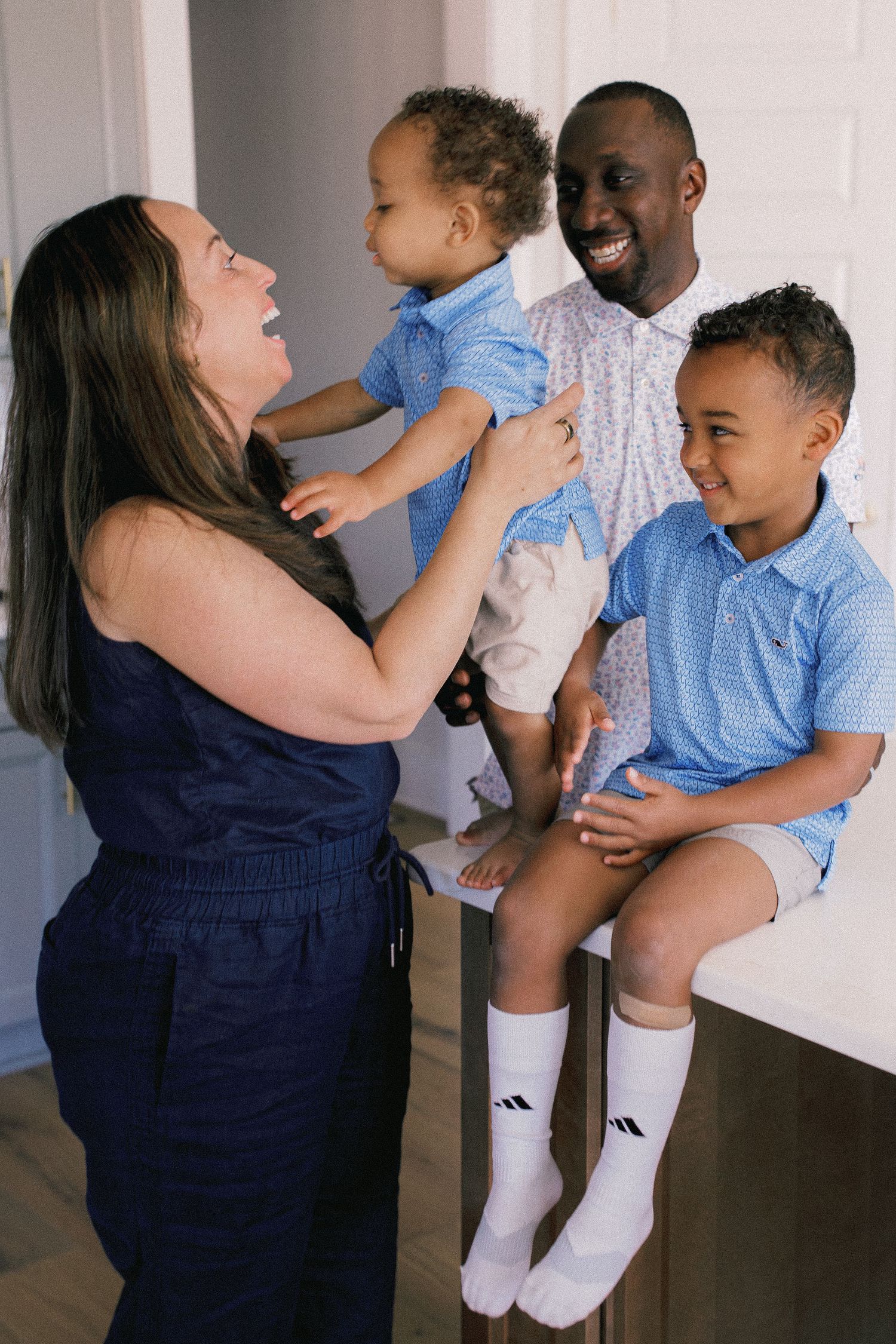 A joyful interracial family of four sharing a happy moment, with two young boys in matching blue polo shirts.