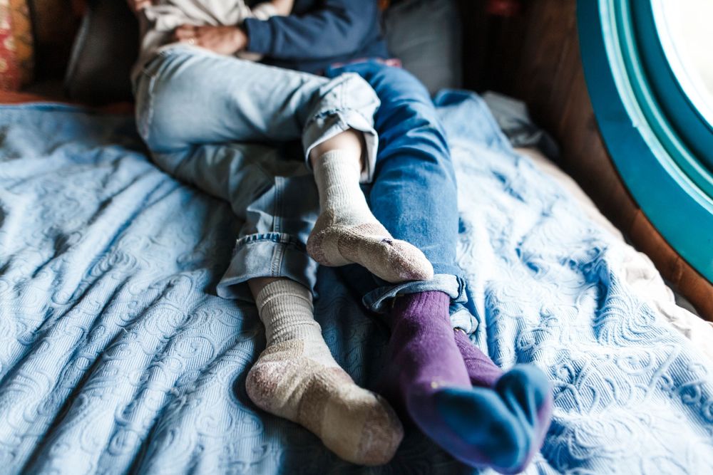Two children lying on a blue blanket wearing colorful socks, cozy indoor scene with natural light.