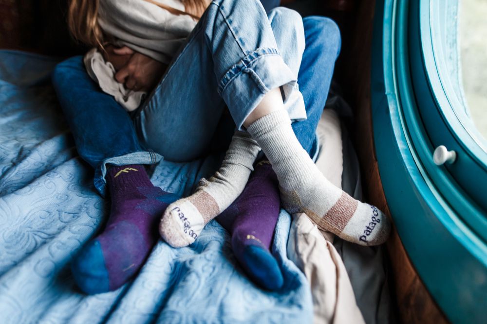Two people relaxing in a train cabin wearing colorful STANCE socks, lounging on blue bedding near a window.