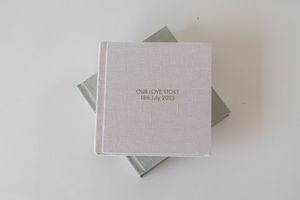 Elegant linen wedding photo album with gold embossed text reading Our Love Story, presented in a matching gift box.