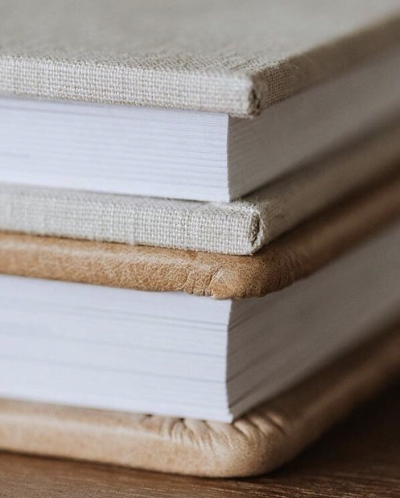 Stack of three hardcover books with linen and leather covers on a wooden surface.