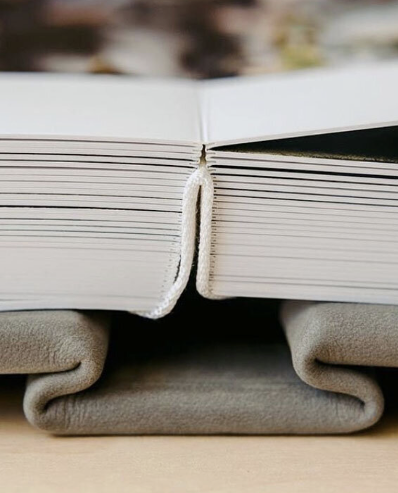 Two open photo books with white pages and leather spines resting on folded gray fabric on a wooden surface.